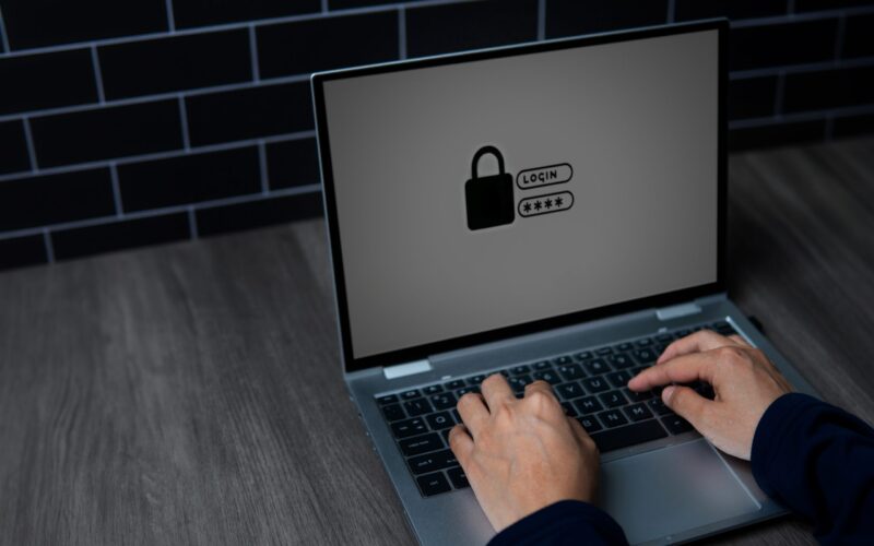 A close-up image of a person's hands typing on a laptop keyboard with a lock symbol on the screen. Cyber security and digital security concept.