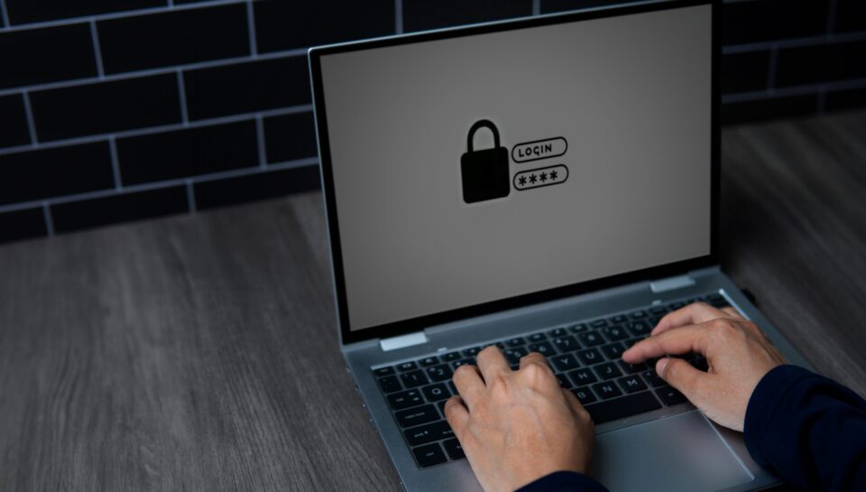 A close-up image of a person's hands typing on a laptop keyboard with a lock symbol on the screen. Cyber security and digital security concept.